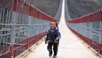 Seorang anak berjalan di jembatan yang membentang di Sungai Niulan di China barat daya ini. Foto: Dok. Xinhua/Yang Wenbin