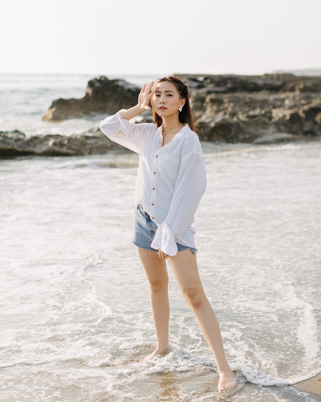 Gaya kasual Shania saat bersantai di pantai: rok pendek denim dan kemeja putih longgar. (Foto: Instagram/@shanju)