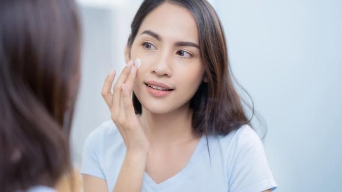 sunscreen Suntan lotion. Woman applying sunscreen solar cream on face. Beautiful happy cute girl puts suntan cream from plastic container bottle on her nose and cheecks. Skincare concept. Female in straw hat and bikini on beach.