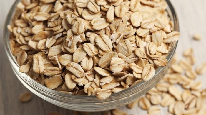 makanan turunkan berat badan Close-up of a small glass bowl filled with rolled oats. The oats are overflowing out of the bowl and have spilled onto the surface next to the bowl. The bowl has rings around the edge, and the oats are raw and in a dry form.