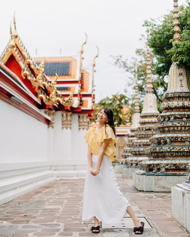 Gaya liburan Shania di Bangkok. Ia mengandalkan blus ruffle dan rok putih panjang maxi, berikut sliders hitam beraksen pita. Cute! (Foto: Instagram/@shanju)