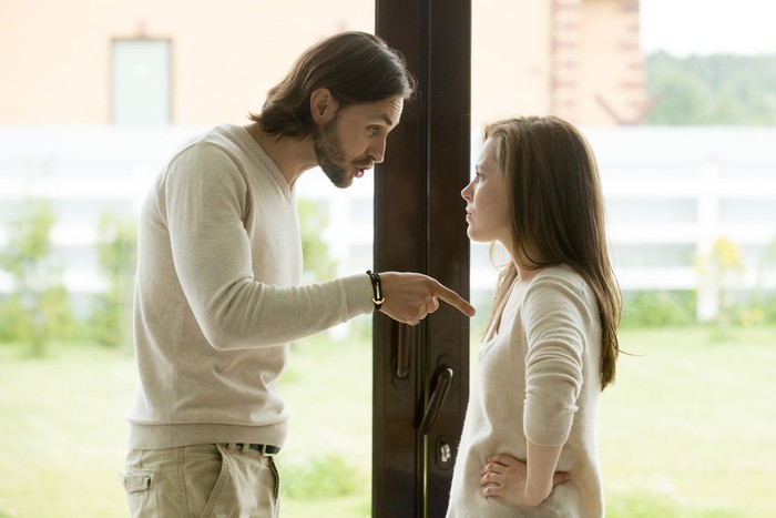 Unhappy young couple arguing standing at house door, angry husband pointing at wife blaming her of problems, conflicts in marriage, bad relationships, man and woman having quarrel or disagreement