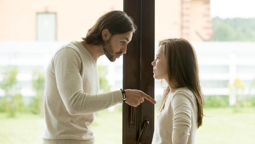 Unhappy young couple arguing standing at house door, angry husband pointing at wife blaming her of problems, conflicts in marriage, bad relationships, man and woman having quarrel or disagreement