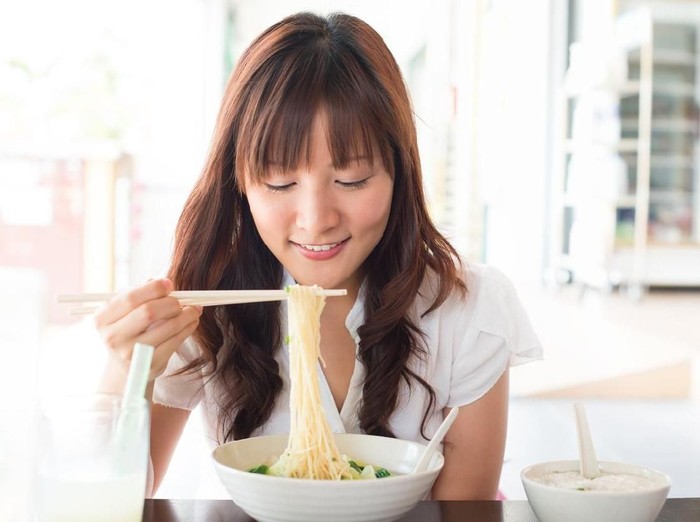 Eating noodles at restaurant. Young Asian girl eating ramen noodles using chopsticks.