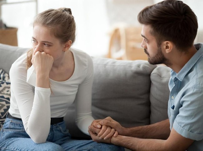 Loving young husband hold crying wife hand showing empathy and support, millennial couple sit on couch at home reconcile after fight, caring man making peace with beloved woman. Relationships concept