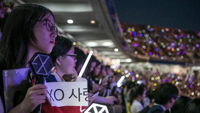 SUWON, SOUTH KOREA - JUNE 18:  A South Korean fan (L) of a boy band, Exo, (not shown) holds a banner as a K-Pop band perform on stage on June 18, 2016 in Suwon, South Korea.The particular concert was organized by the city government of Suwon, commemorating the 220th anniversary of Suwon-Hwaseong Fortress, a UNESCO heritage site. It featured 25 K-Pop idol groups and solo artists for two days: June 17 and 18, 2016, drawing more than 10,000 visitors. The South Korean government, both on a central and local level, try to boost tourism by sponsoring and directly organizing K-Pop concerts in big venues. The fans come from Korea as well as Japan, China, and Southeast Asia, as the popularity of K-pop had rapidly grown after it started in Japan in the early 2000s, and expanded its fan base to teenagers and young adults in China, Southeast Asia, and as far as Latin America.  (Photo by Jean Chung/Getty Images)