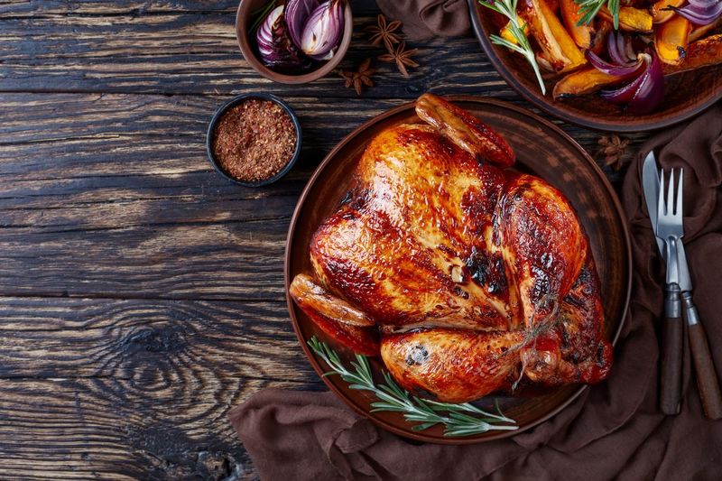 whole roasted chicken with golden brown crispy skin served on a earthenware dish with caramelized grilled pumpkin slices and grilled onion, view from above, flat lay, copy space