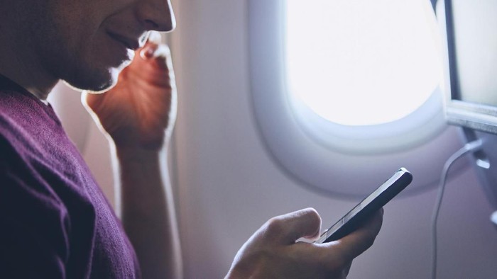Connection during flight. Young man using mobile phone in airplane.