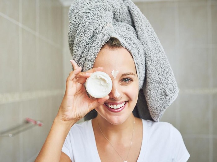 Portrait of an attractive young woman applying moisturizer to her face at home