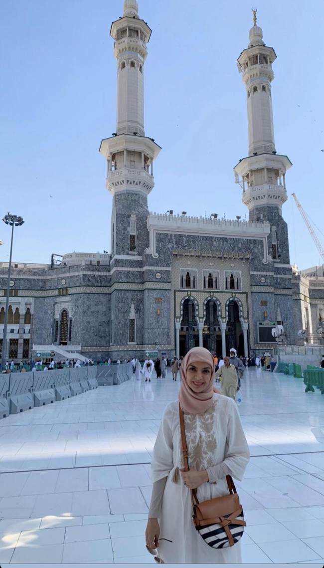 Tampil sederhana saat umrah, pembawa acara berita yang dikenal dengan sikap tegas ini mengenakan hijab segi empat. Najwa Shihab menggunakan hijab warna pink pastel yang dililit rapi ke belakang dan gamis warna putih dengan manset. Foto: instagram @najwashihab