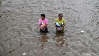 Dua orang warga menyeberangi jalan yang terendam banjir.