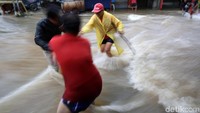 Beberapa warga berusaha melewati derasnya arus air di jalan utama Komplek Duta Indah.