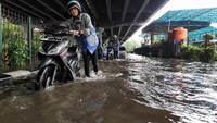 Pengendara mendorong motornya yang mogok saat menerobos banjir.