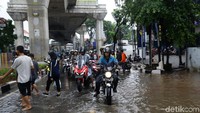 Pengendara sepeda motor mengantre untuk melintas di jalan yang terendam banjir.