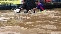 Pemotor mendorong motornya yang mogok akibat menerobos banjir.