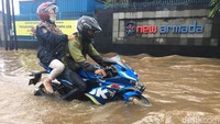 Pengendara sepeda motor menerobos derasnya arus banjir.
