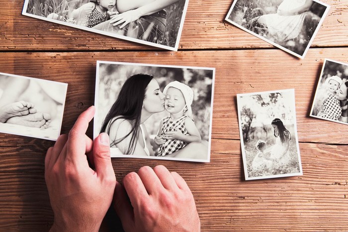 Ibu dan anak Mothers day composition. Hands of unrecognizable man holding black-and-white photo. Studio shot on wooden background.