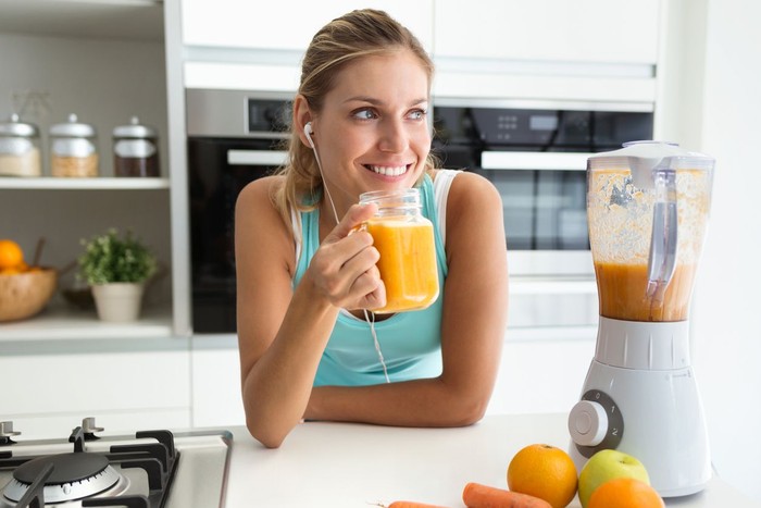 jus Shot of beautiful sporty young woman looking sideways and drinking vegetable detox juice in the kitchen at home.