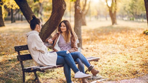Two female friends talking on a bench in autumn park