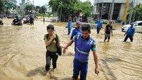 Seorang petugas tampak membantu seorang warga yang ingin menerobos banjir.