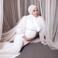 Foto kehamilan selanjutnya, Biby yang mengenakan dress putih berpose duduk sambil menyentuh perutnya. Wanita 29 tahun itu menggunakan hijab dua layer dan diikat pita di bagian bawah lehernya. Foto: instagram @bibyalraen13
