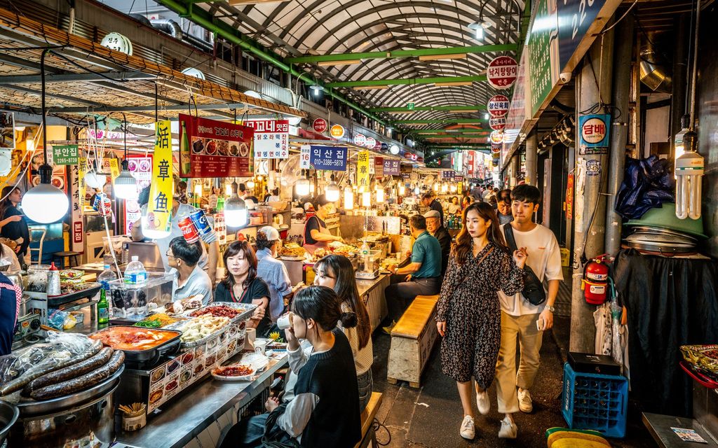 Seoul, South Korea - 29th April 2013: Local people sitting and eating traditional Korean food at a crowded street food stall served by a woman trader in the vibrant and lively Dongdaemun Market in the heart of downtown Seoul, Korea.