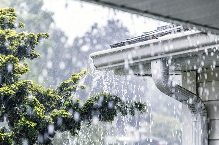 Boy stands outside as the rain pours down. He sticks out his tongue to taste the water falling from the sky.