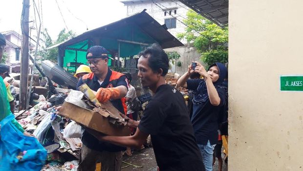 Anies dibantu warga mengangkat sampah kayu.
