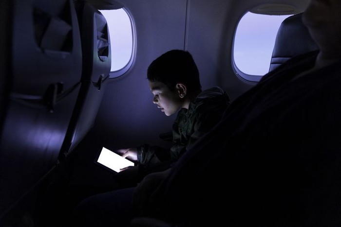 High quality stock photo of a young boy playing and using a tablet computer on an airport plane.