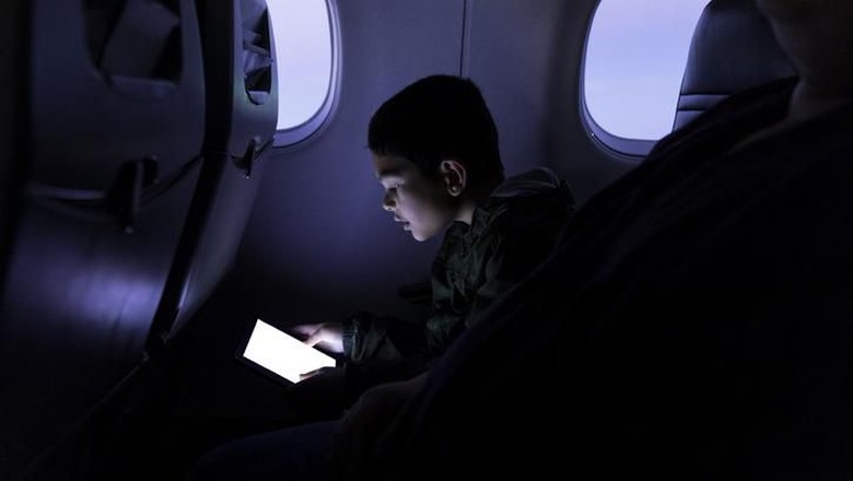 High quality stock photo of a young boy playing and using a tablet computer on an airport plane.