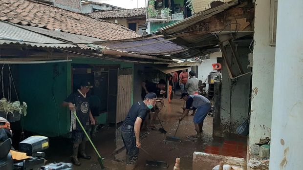 Warga dan petugas bekerja sama membersihkan lumpur sisa banjir.