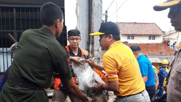 Anies dibantu warga mengangkat karung berisi sampah.