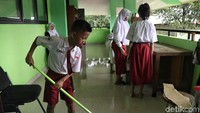 Dengan menggunakan peralatan yang tersedia, para siswa membersihkan lantai di area-area sekolah usai banjir merendam sekolah tersebut.