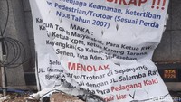 Sebuah spanduk berisi penolakan trotoar digunakan oleh pedagang kaki lima (PKL) terpasang di Jalan Salemba Raya, Jakarta Pusat. Diketahui, spanduk itu dipasang oleh warga sekitar yang terganggu karena trotoar untuk pejalan kaki diserobot oleh PKL. (Foto: Yogi Ernes/detikcom)