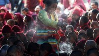 Seorang wanita budha berkeliling menyalakan dupa ketika para biksu membacakan kitab.