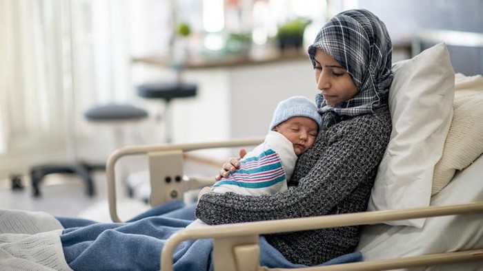 doa untuk anak bayi baru lahir A Muslim woman is laying in a hospital bed. She is holding her newborn son on her lap. She is watching over her baby while he sleeps.