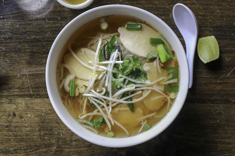 Happy Vietnamese children eating a pho bo in local restaurant, next to the road, South Vietnam. Pho bo is a extremely popular Vietnamese noodle soup consisting of broth, rice noodles, herbs and beef meat.