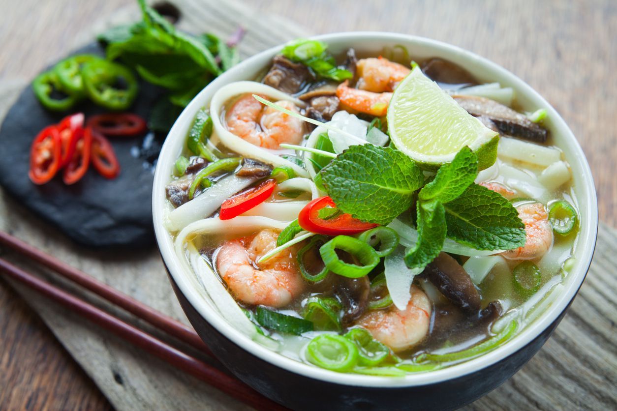 Happy Vietnamese children eating a pho bo in local restaurant, next to the road, South Vietnam. Pho bo is a extremely popular Vietnamese noodle soup consisting of broth, rice noodles, herbs and beef meat.