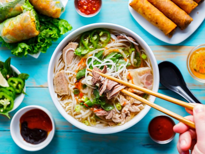 Happy Vietnamese children eating a pho bo in local restaurant, next to the road, South Vietnam. Pho bo is a extremely popular Vietnamese noodle soup consisting of broth, rice noodles, herbs and beef meat.