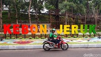 Driver Ojol melintas di depan papan nama Taman Kebon Jeruk.