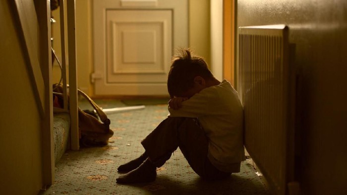 sad child with his head between his legs left alone at home