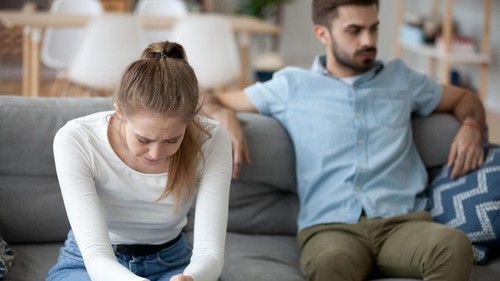 Unhappy young millennial married couple sitting on couch in living room after quarrel fight. Angry husband frustrated offended wife at home. Break up, divorce and misunderstanding in relations concept