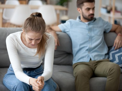 Unhappy young millennial married couple sitting on couch in living room after quarrel fight. Angry husband frustrated offended wife at home. Break up, divorce and misunderstanding in relations concept