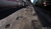 Pemotor melintas di jalan yang penuh lubang.