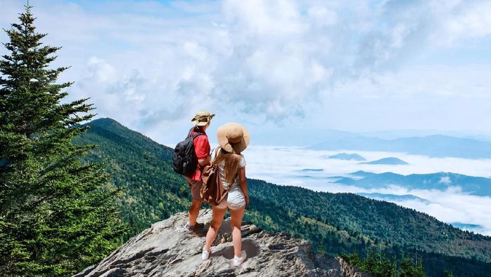 Couple on hiking trip, standing on top of the mountain over the clouds, looking at beautiful summer mountain  landscape. People enjoying beautiful view. Close to Asheville, North Carolina, USA.