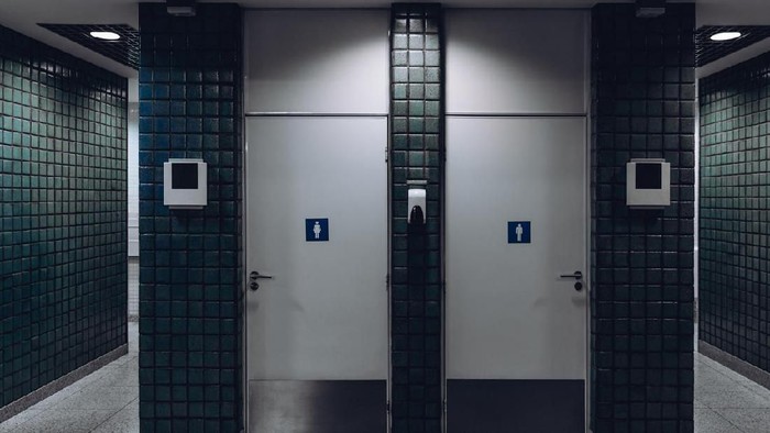 Dark public toilet entrances for men and for women in a modern airport terminal building or railway station depot, with greenish ceramic tiles on the wall: two dors and two more entrances