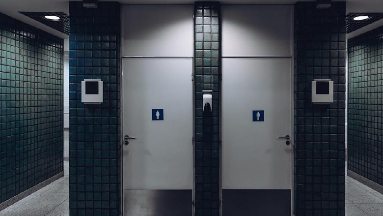 ilustrasi toilet bandara Dark public toilet entrances for men and for women in a modern airport terminal building or railway station depot, with greenish ceramic tiles on the wall: two dors and two more entrances