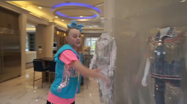 Begitu masuk rumah, langsung terpampang tangga spiral serta grand piano. Area ini juga menjadi semacam galeri yang memperlihatkan kostum-kostum yang pernah dikenakan Jojo Siwa saat konser. Foto: Screenshot YouTube/ Its Jojo Siwa