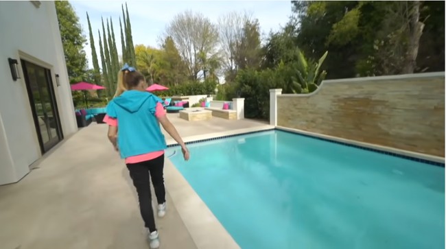 Area kolam renang dilengkapi sofa dan meja serta tenda payung berwarna-warni khas Jojo Siwa, yakni biru muda dan pink. Foto: Screenshot YouTube/ Its Jojo Siwa