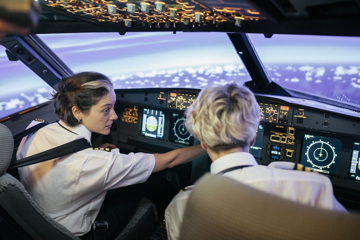A flight instructor is describing various dials and displays to a trainee pilot in the cockpit of a simulator.